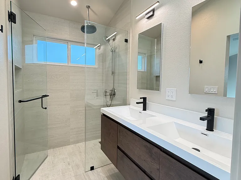 Primary suite bathroom with hanging dual vanity, large curbless stall shower with custom niche and frameless shower door.