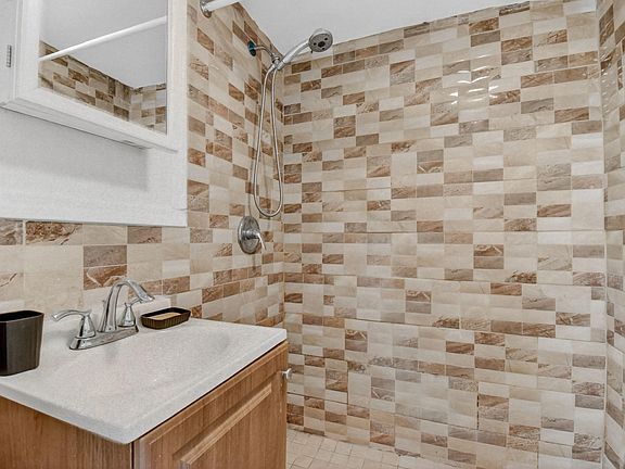 Bathroom with tiled tub/shower surround, vanity sink, and mirrored medicine cabinet for everyday storage.