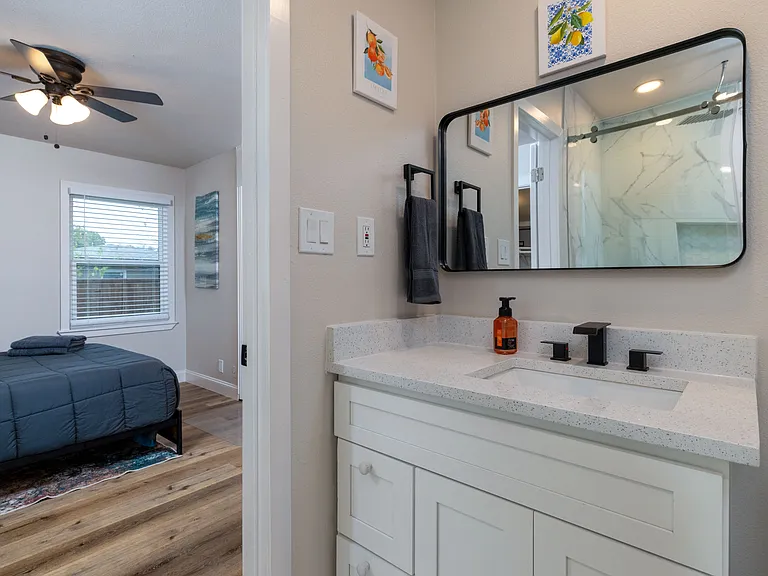 Relax in a modern, spa-style bathroom with a marble-tiled walk-in shower, sleek black fixtures, bright vanity lighting, and clean finishes. Directly connected to the primary bedroom for privacy and convenience.