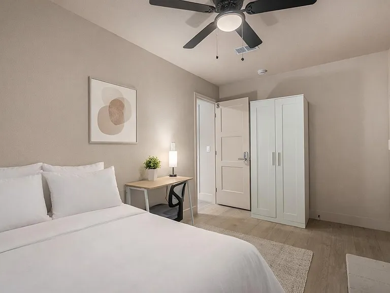 Queen bed, desk, chair, lamp, fan, closet. Bedding and rug are virtually staged.