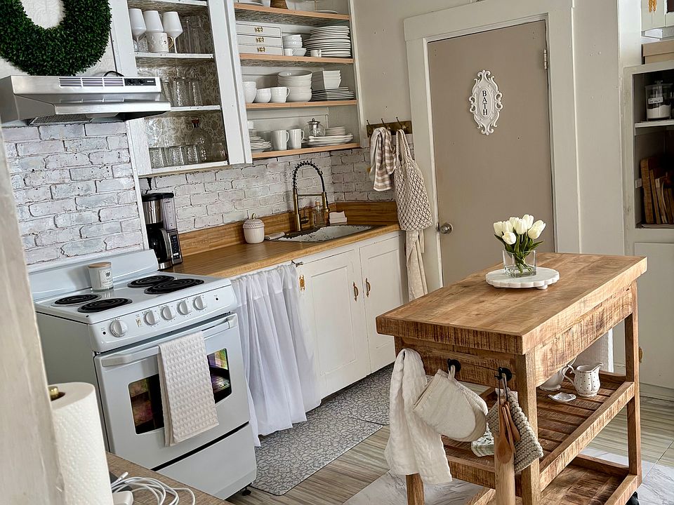 This Scandinavian kitchen combines old-fashioned cottage core design with modern fixtures. The farmhouse style is inviting with open shelving, and linen cabinet coverings bring a cozy feel to this space. (New flooring not shown in this photo)