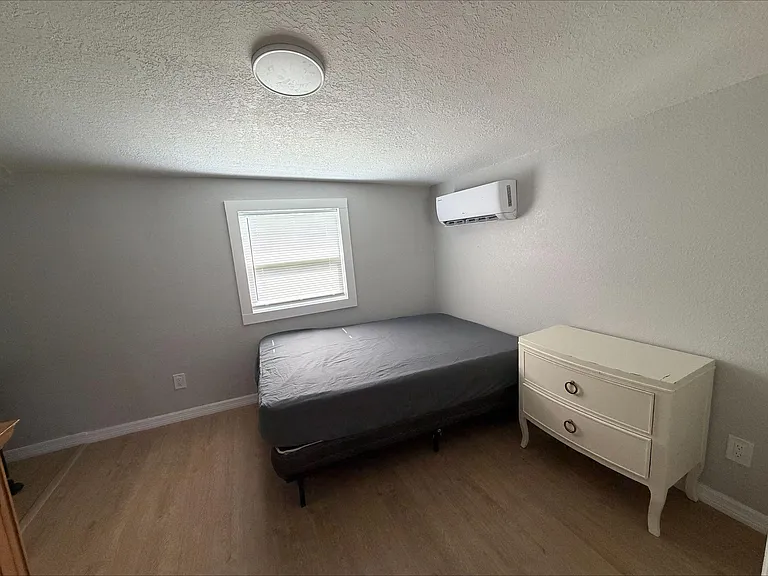Private bedroom with a window for natural light, a bed, and a convenient nightstand, plus a wall-mounted mini-split AC.