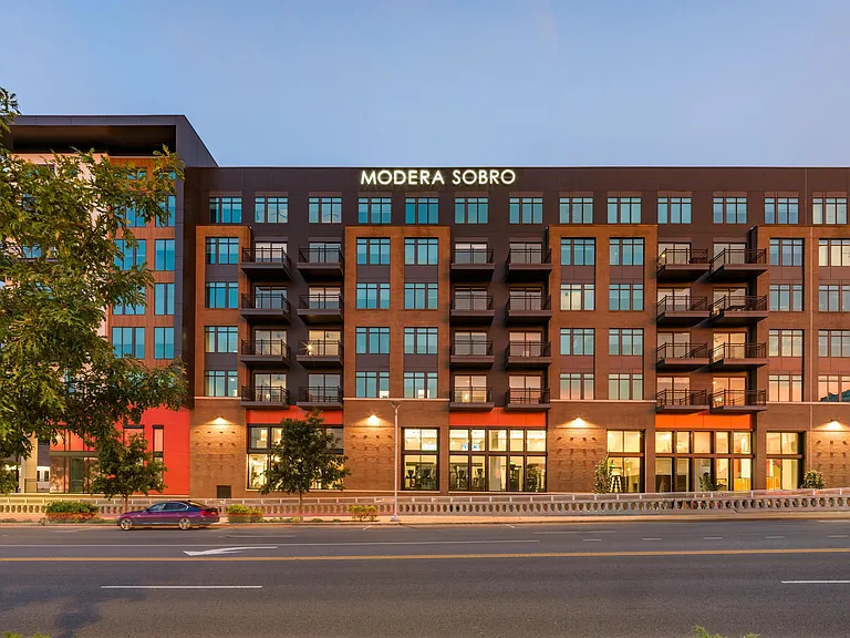 Twilight view of Modera SoBro's exterior, featuring a bold mix of brick and dark paneling with private balconies and expansive windows.