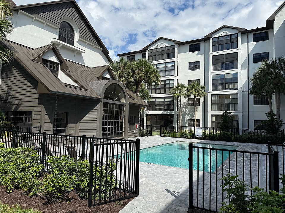 Charming apartment complex with a refreshing pool, modern architecture, and lush palm trees under a bright blue sky.