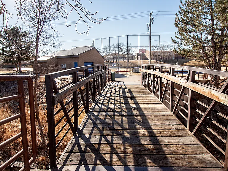Charming pedestrian bridge leading to a serene park area, with rustic wooden planks and metal railings, perfect for nature walks and outdoor relaxation.