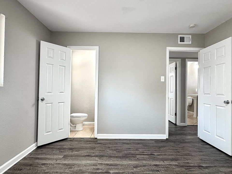 Bright and spacious bedroom featuring sleek wood flooring, neutral gray walls, and convenient access to a modern ensuite bathroom.