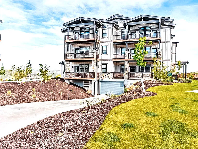 Modern condo building exterior featuring private balconies, stone and board-and-batten siding, and well-manicured grounds