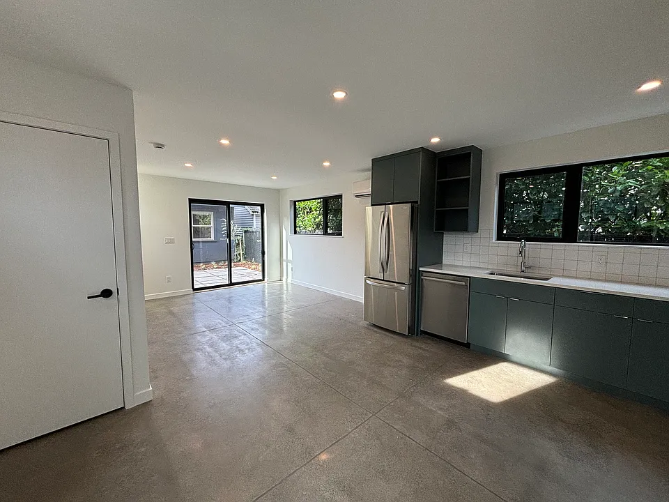 Open floor plan with full kitchen, dishwasher, concrete floors. Washer/dryer units behind door.