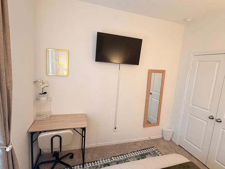 Bedroom corner with wall-mounted TV, work desk, and full-length mirror next to the closet door.