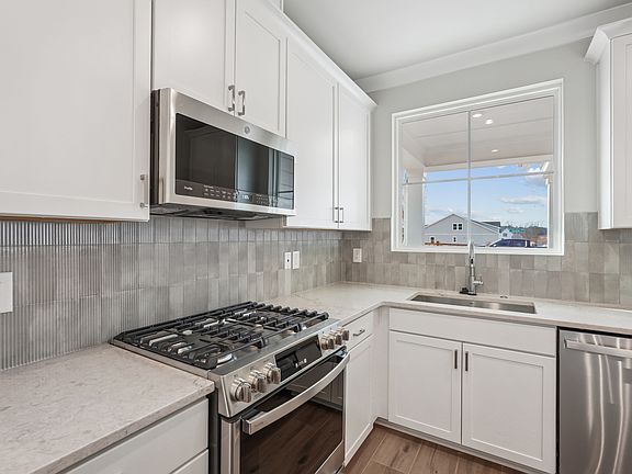 A modern, well-equipped kitchen with white cabinets, stainless steel appliances, and a tiled backspl