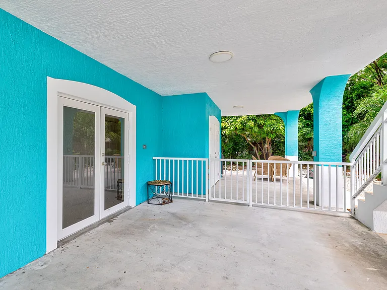 Outdoor access door under carport french door with private laundry room and some storage on the left behind the white fence.