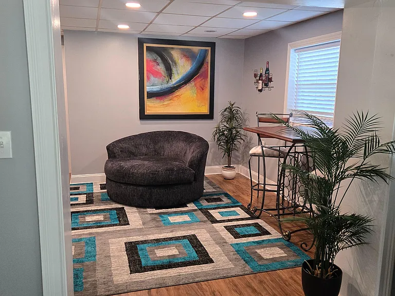 Inviting common lounge area with comfortable seating, accent art, and a bistro table beside a window with blinds.