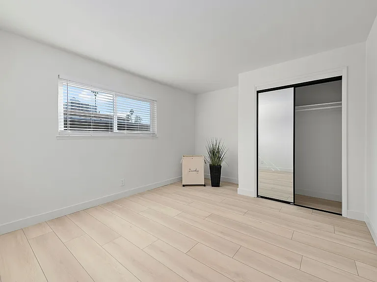 A generously sized bedroom with mirrored closet doors that add brightness and a sense of expanded space.