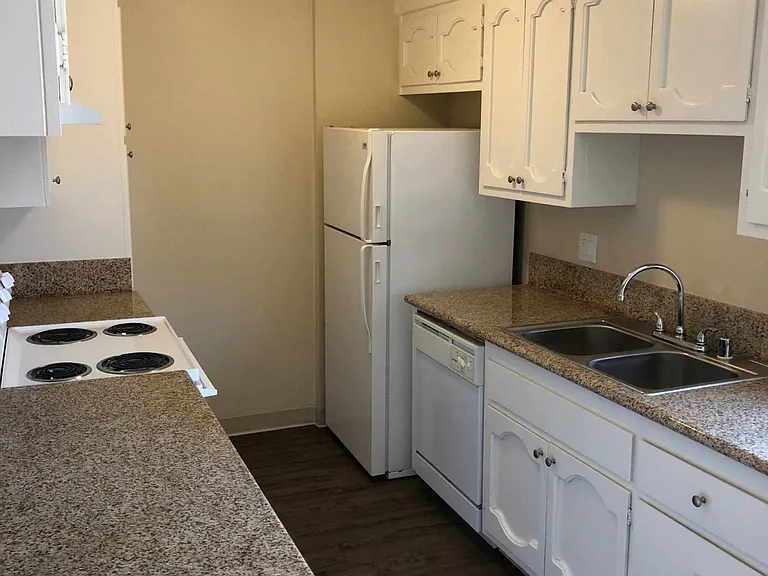 Kitchen with spacious white cabinets, plank style flooring, refrigerator, dishwasher, microwave, and electric stove at Plaza Verde Apartments in Escondido, California.