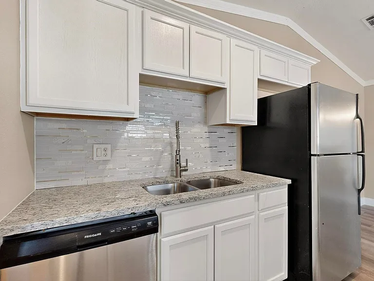Kitchen featuring decorative backsplash, appliances with stainless steel finishes, white cabinetry, ornamental molding, and vaulted ceiling