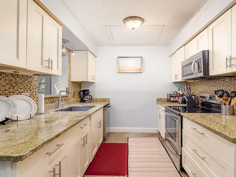 Galley kitchen with generous granite counters, ample cabinet storage, mosaic tile backsplash, and stainless appliances.