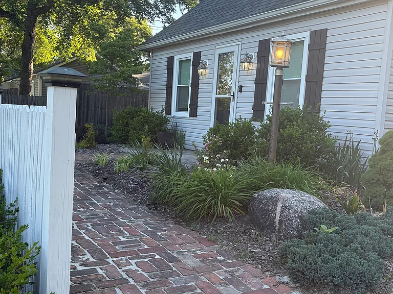 A charming brick walkway leads to the front door, framed by flowering and evergreen landscaping.