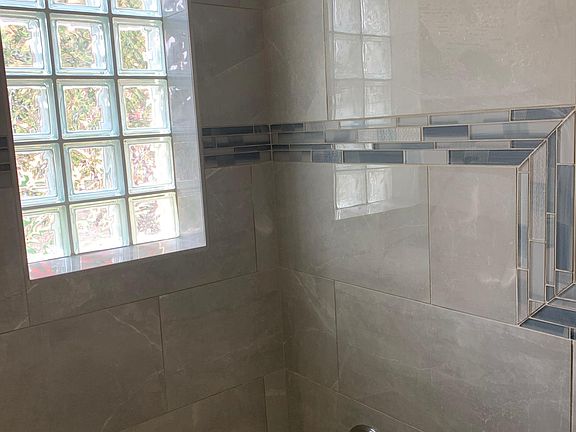 This gorgeous full bath features grey marble wainscoting, blue glass accent tile, pewter, white, and grey tile plank floors, a glass-blocked window, modern vanity light, and a new vanity, faucets, and toilet. Once the walls are painted and the mirror and