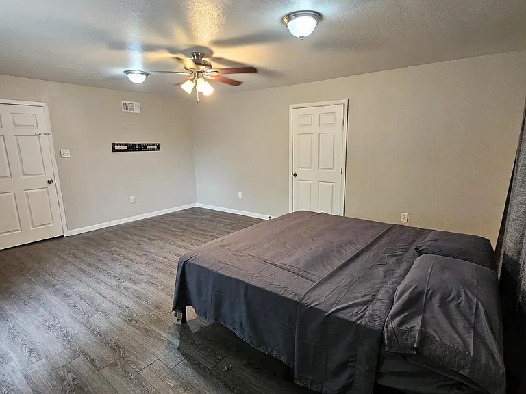 Spacious bedroom with wood-look flooring, ceiling fan, and ample wall space, plus convenient closet and room for a full bed.