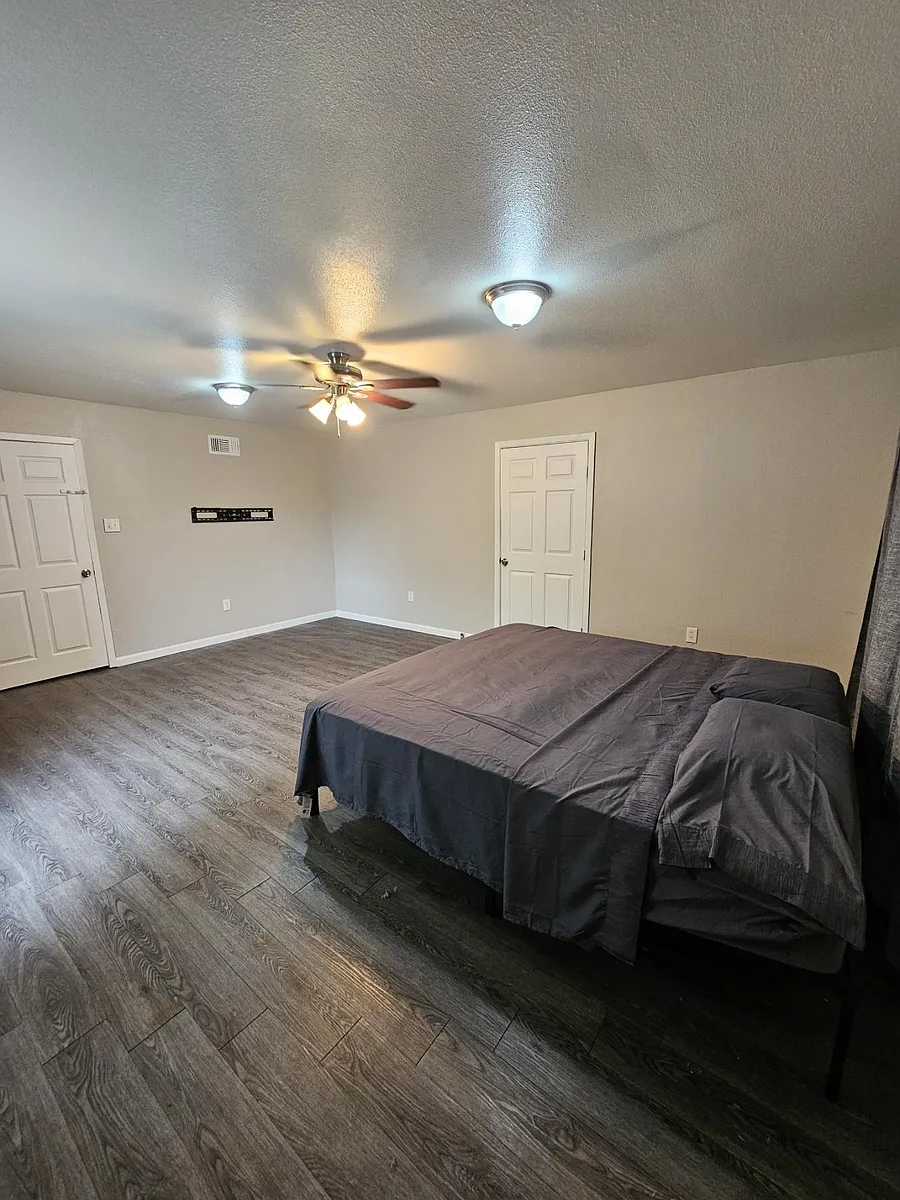Spacious bedroom with wood-look flooring, ceiling fan, and ample wall space, plus convenient closet and room for a full bed. - Glenda St