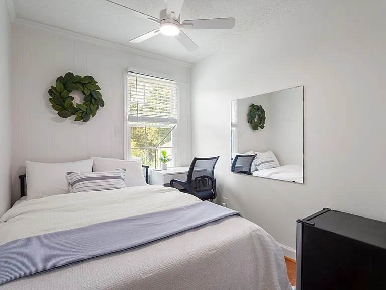 Well-appointed bedroom with a full bed, ceiling fan, work desk, and window with blinds for natural light and privacy.
