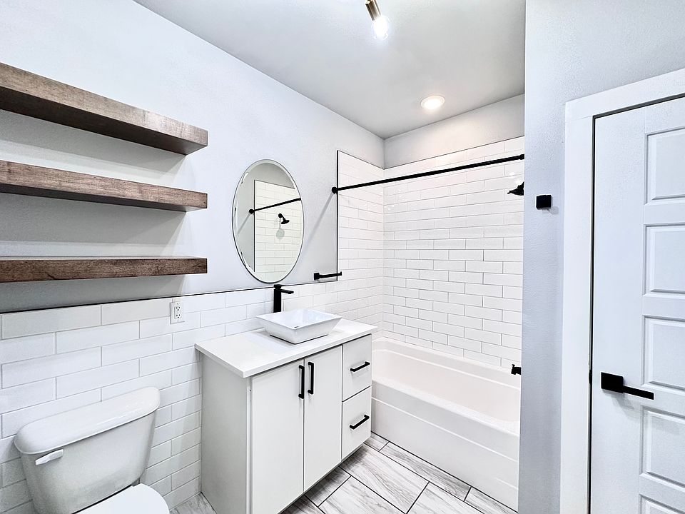 A bathroom that blends modern and rustic charm with statement lighting, tiled backsplash and natural wood shelving for a clean, organic feel. Call or text for a tour today!