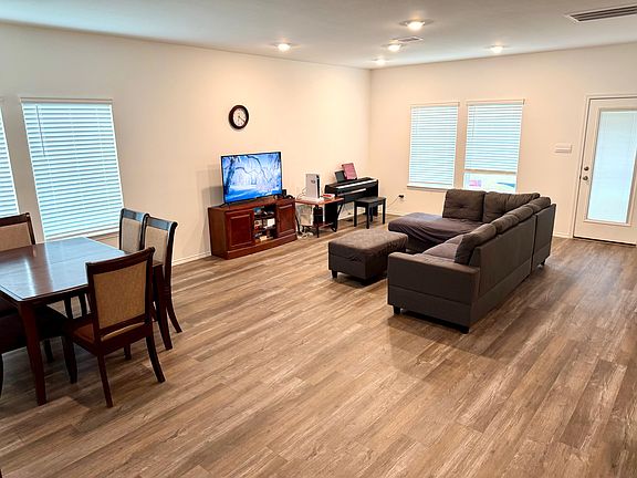 Open-concept living area with sectional seating, TV setup, and adjacent dining space, plus a door to the outside.