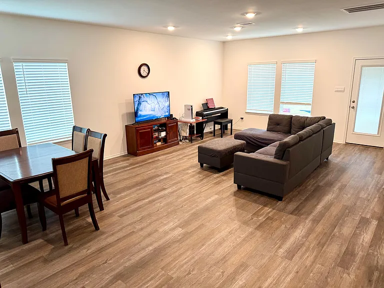 Open-concept living area with sectional seating, TV setup, and adjacent dining space, plus a door to the outside.