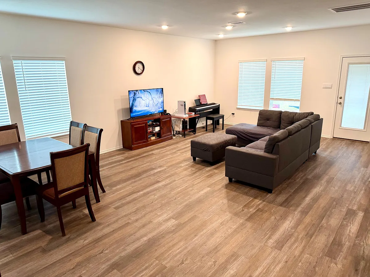Open-concept living area with sectional seating, TV setup, and adjacent dining space, plus a door to the outside. - Eastern Pine Trl