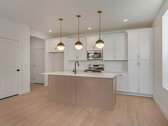 Modern kitchen with a central island, three pendant lights, white cabinets, stainless steel applianc