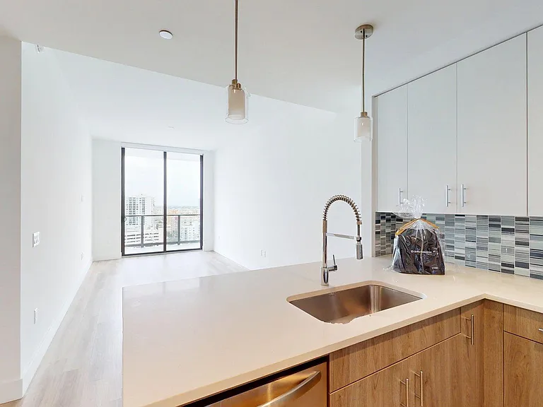 Apartment Kitchen with Stainless Steel Appliances, white stone countertops and wood-style floors.