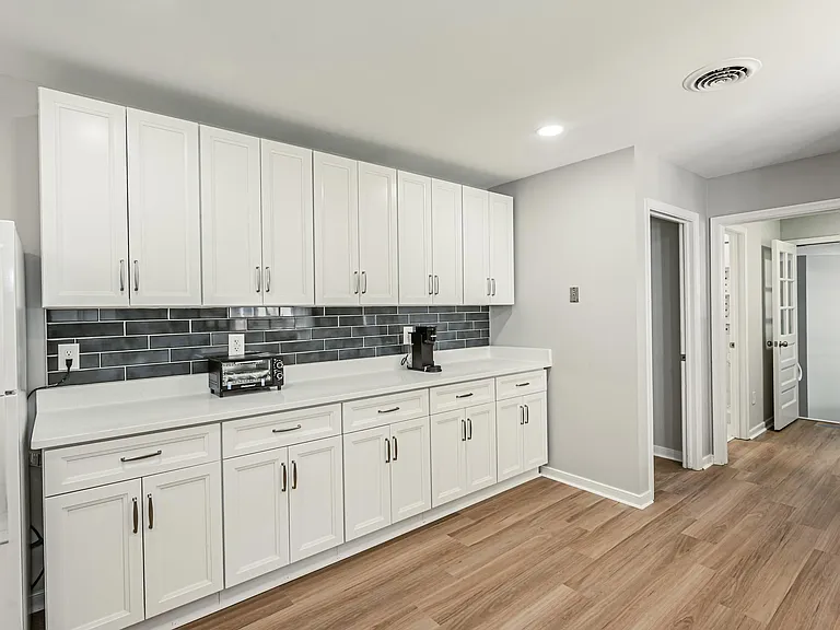 Kitchen with extensive white cabinetry, long counter space, and a tile backsplashideal for meal prep and storage.