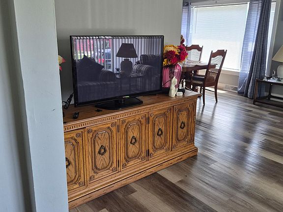 Open common area with durable wood-look flooring, space for lounging, and a dining nook set beside a large window.