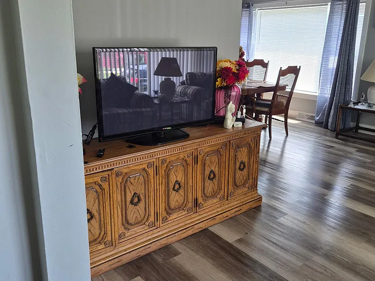 Open common area with durable wood-look flooring, space for lounging, and a dining nook set beside a large window.
