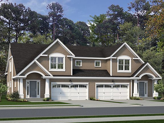 A duplex with beige siding, white trim, and dark brown roofs, featuring two garages with white doors