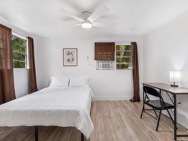Private bedroom with a full bed, closet storage, and a dedicated desk space beside a window with wooded views.
