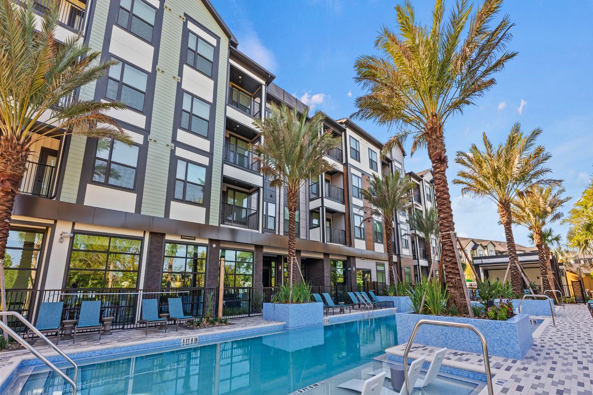 Luxurious apartment complex with sleek modern design, palm trees, and an inviting swimming pool featuring in-water lounge chairs.