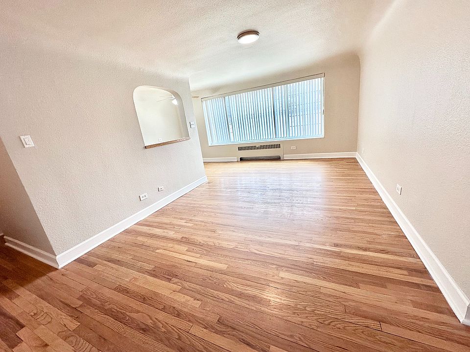 Bright and spacious living area with polished hardwood floors, large window, and sleek archway adding modern charm.