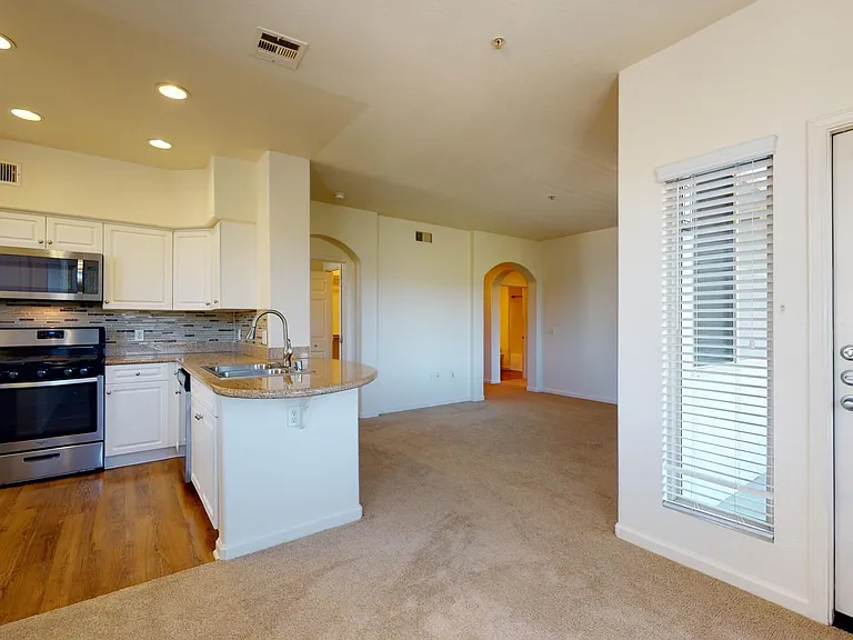 Apartment kitchen with stainless steel appliances, dining and living room with plush carpet flooring.