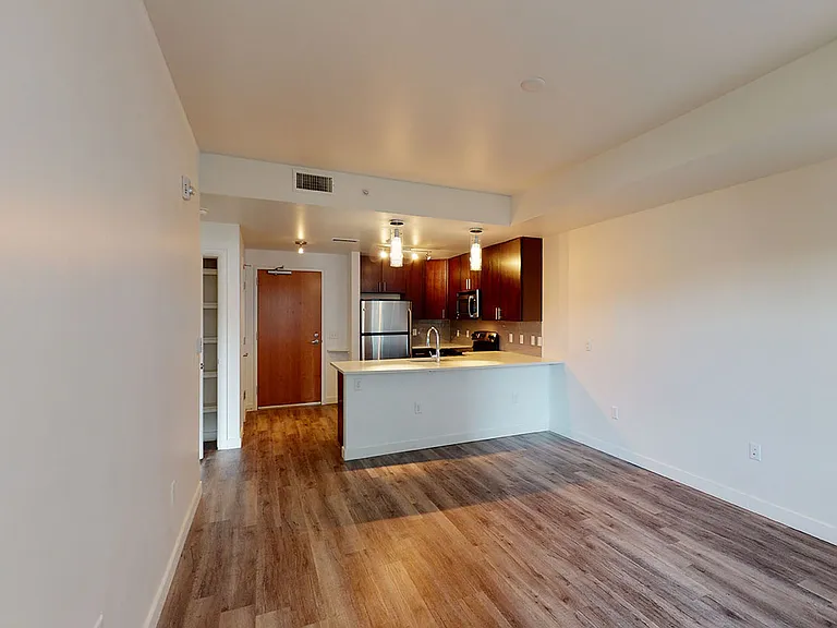 Apartment kitchen with stainless steel appliances, dining and living room with wood-style flooring.