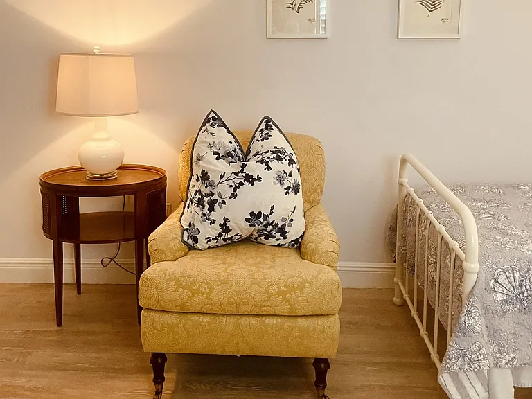 Quiet sitting corner inside the private bedroom. Beautifully appointed with traditional designer seating, timeless wood finishes, and warm bedside lighting for ultimate comfort.