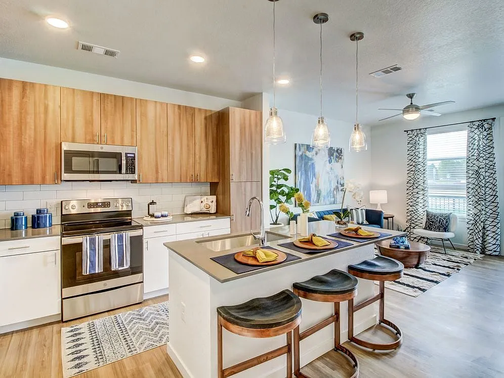 Kitchens feature oak upper and white lower cabinetry, grey quartz countertops, white subway tile backsplash, kitchen island or breakfast bar, and luxury vinyl plank flooring - Avalon Flatirons