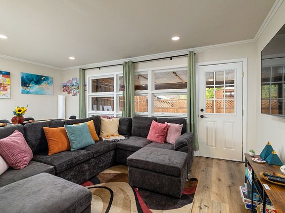 Bright, cozy living room with a large sectional, modern art, big windows, a smart TV, board games, and a DVD collection. Perfect for relaxing, gathering, or getting work done in a stylish, welcoming space.