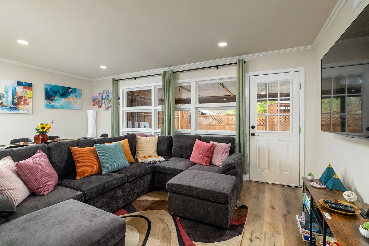 Bright, cozy living room with a large sectional, modern art, big windows, a smart TV, board games, and a DVD collection. Perfect for relaxing, gathering, or getting work done in a stylish, welcoming space. - 2219 Greenway St