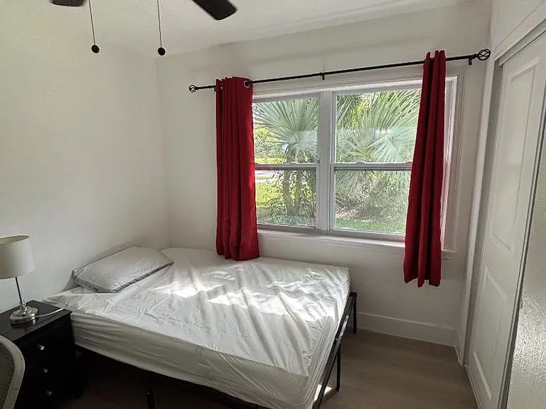 Private bedroom with a large window, ceiling fan, and closet storage, furnished with a bed and nightstand.