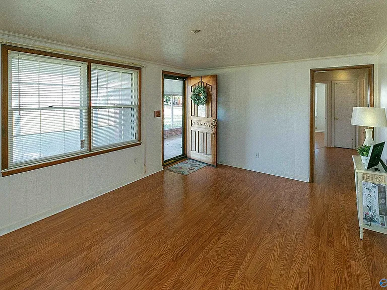 Yet another living room view, this one showing the front window, the front door, and the opening into the hall. The kitchen is to the right.