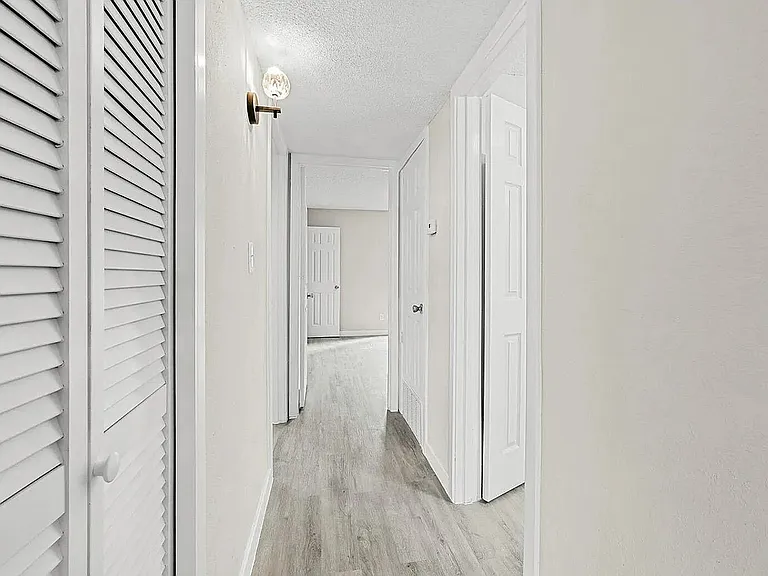 Bright and inviting hallway with modern light fixture, sleek wooden flooring, and crisp white doors, showcasing a stylish apartment interior.