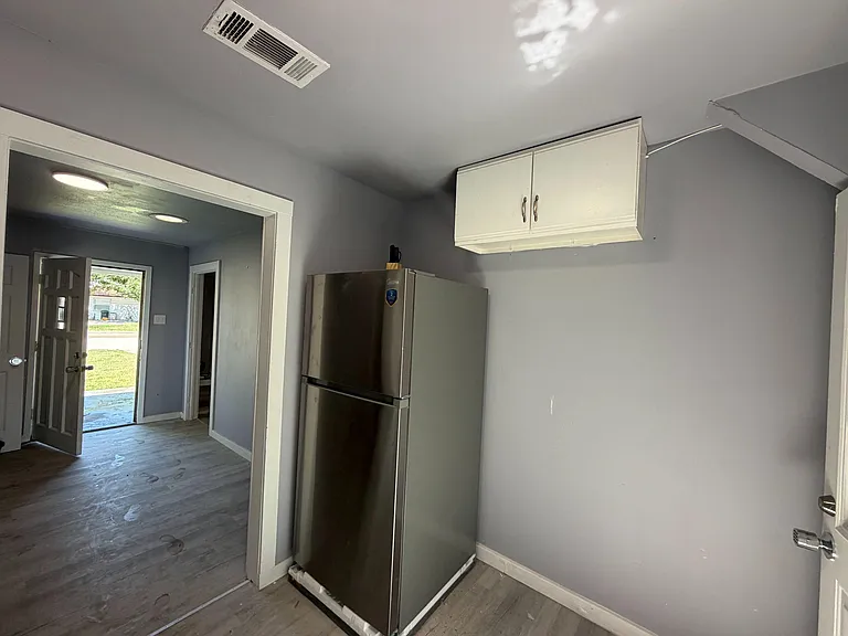 Kitchen area with a stainless refrigerator and upper cabinets, offering convenient storage near the main entry.