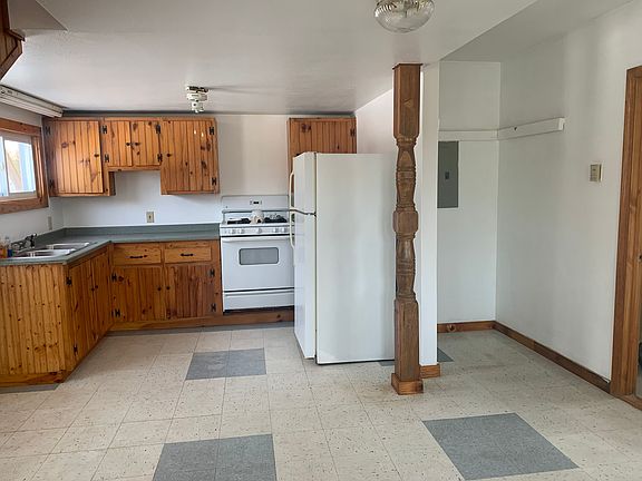 Anover view of living/kitchen, fridge is blocking view of counter and cabinet that extend to wall. Bathroom door on the right side.