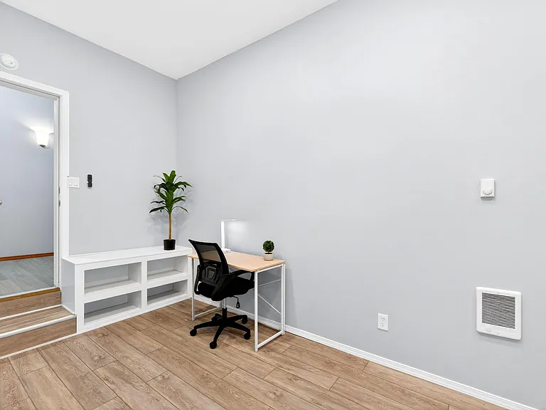 Dedicated work nook with a desk, task lighting, and open shelving, set on durable wood-look flooring near the entry.